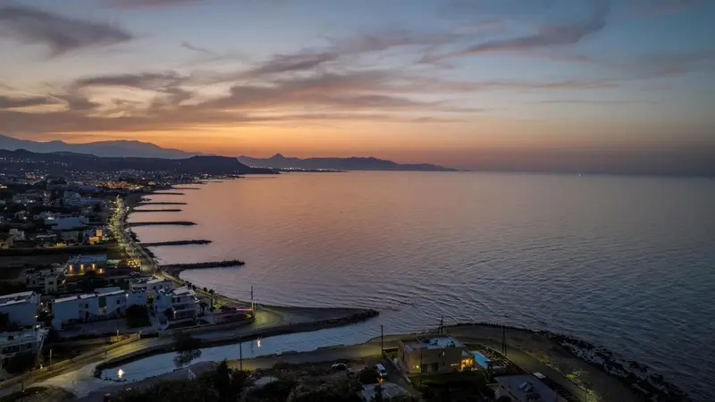 Vue aérienne d'une côte illuminée au coucher du soleil, avec des montagnes en arrière-plan.