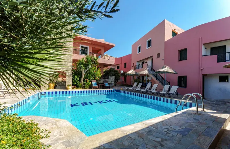 Piscine rectangulaire turquoise devant un bâtiment rose à deux étages.