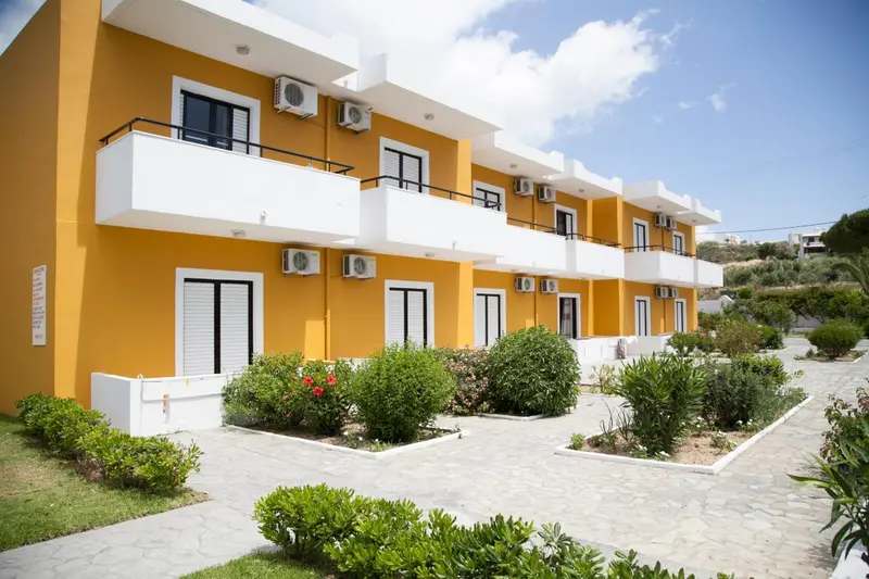 Façade d'un bâtiment jaune à balcons blancs, entouré de végétation.