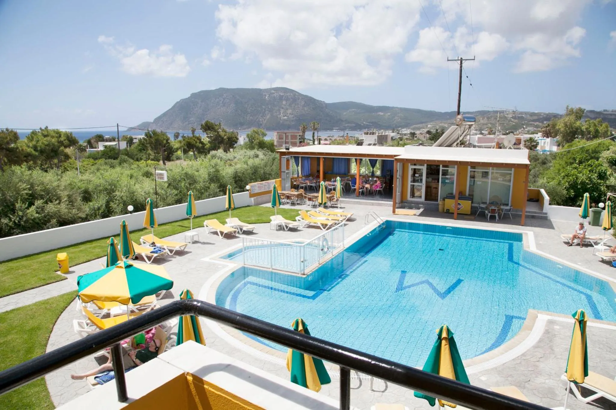 Une piscine bleue bordée de transats et de parasols, avec une vue sur la mer et les montagnes en arrière-plan.