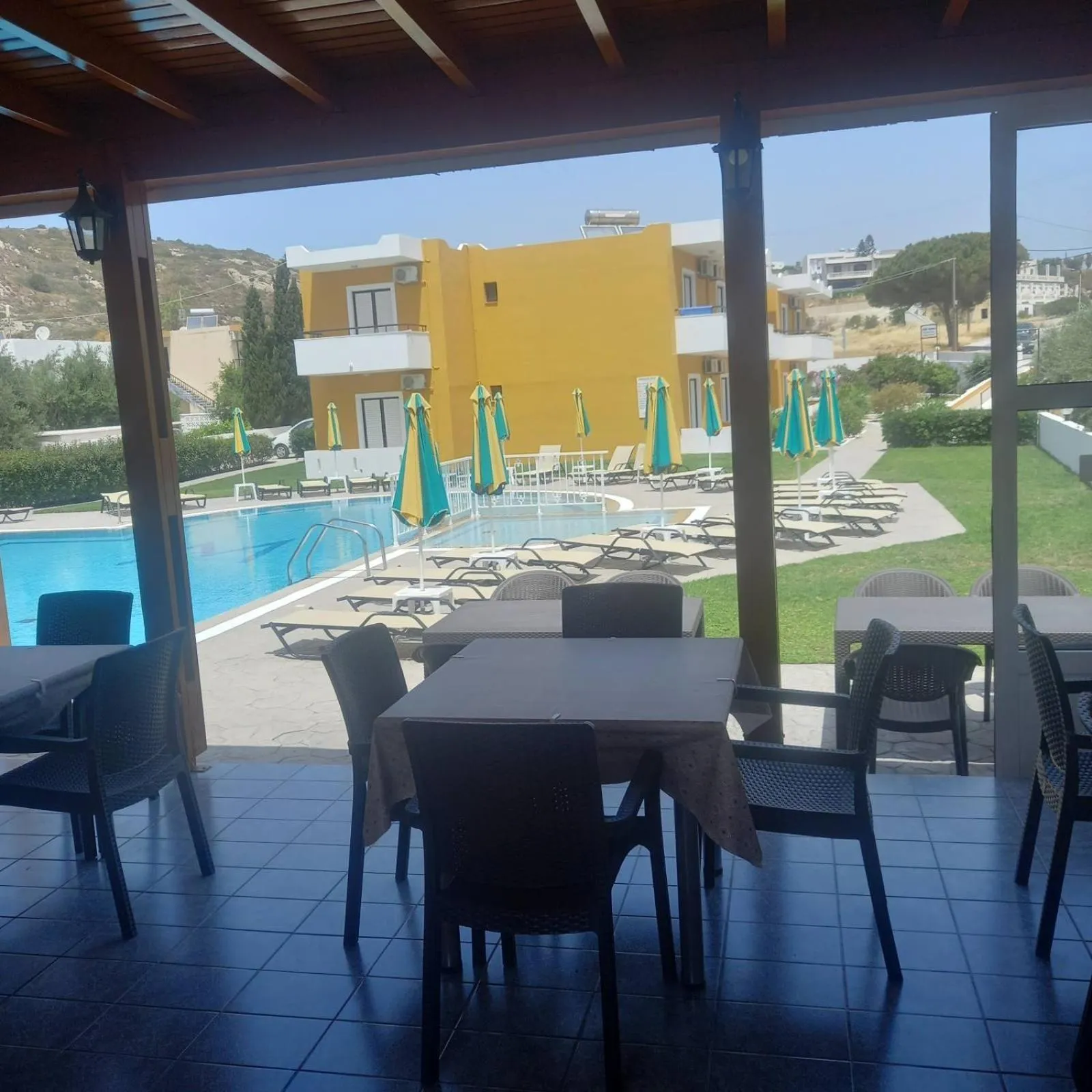 Tables et chaises disposées devant une piscine et un bâtiment jaune.