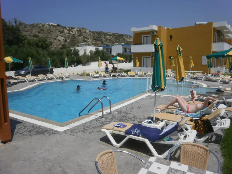 Transats et parasols bordent une piscine ensoleillée avec des personnes se relaxant.