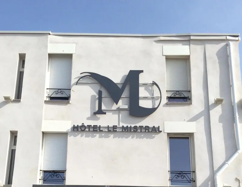 Façade d'un bâtiment blanc avec un grand logo en forme de M et l'inscription d'un nom d'hôtel.
