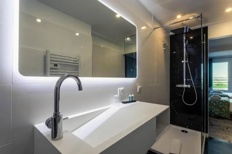 Une salle de bain moderne avec une douche à l'italienne et un grand miroir éclairé.