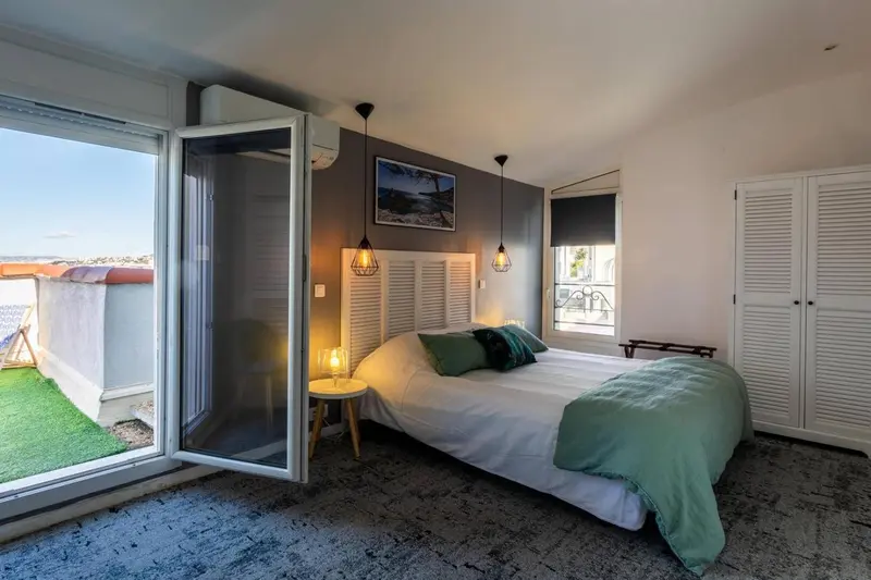 Une chambre lumineuse avec un lit recouvert d'une couverture verte et un accès à une terrasse.