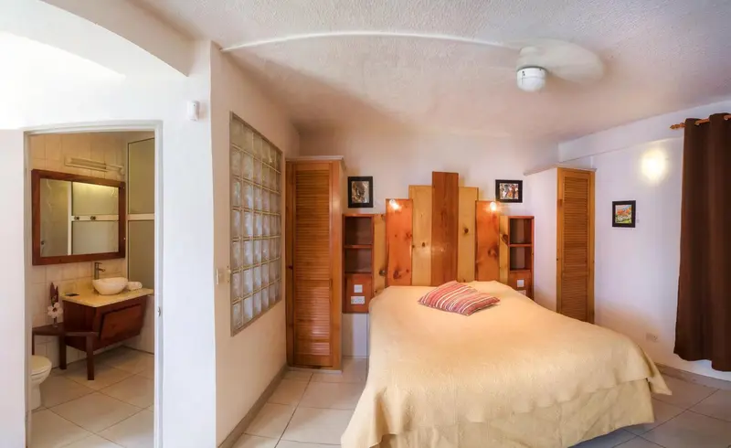 Une chambre lumineuse avec un lit recouvert d'une courtepointe et un coin lavabo.