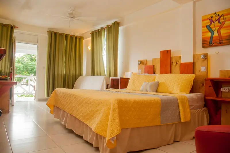 Une chambre lumineuse avec un grand lit recouvert d'une courtepointe jaune et de coussins.