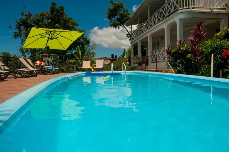 Une piscine rectangulaire turquoise reflète le ciel bleu et la végétation luxuriante.