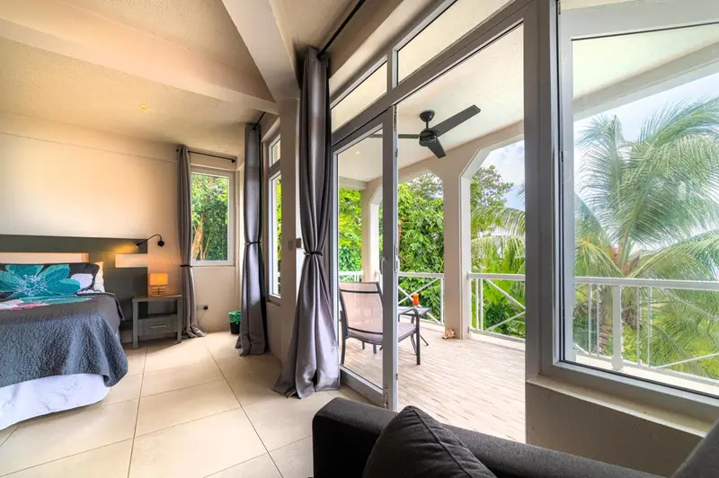 Une chambre lumineuse s'ouvre sur une terrasse ombragée avec vue sur la végétation.