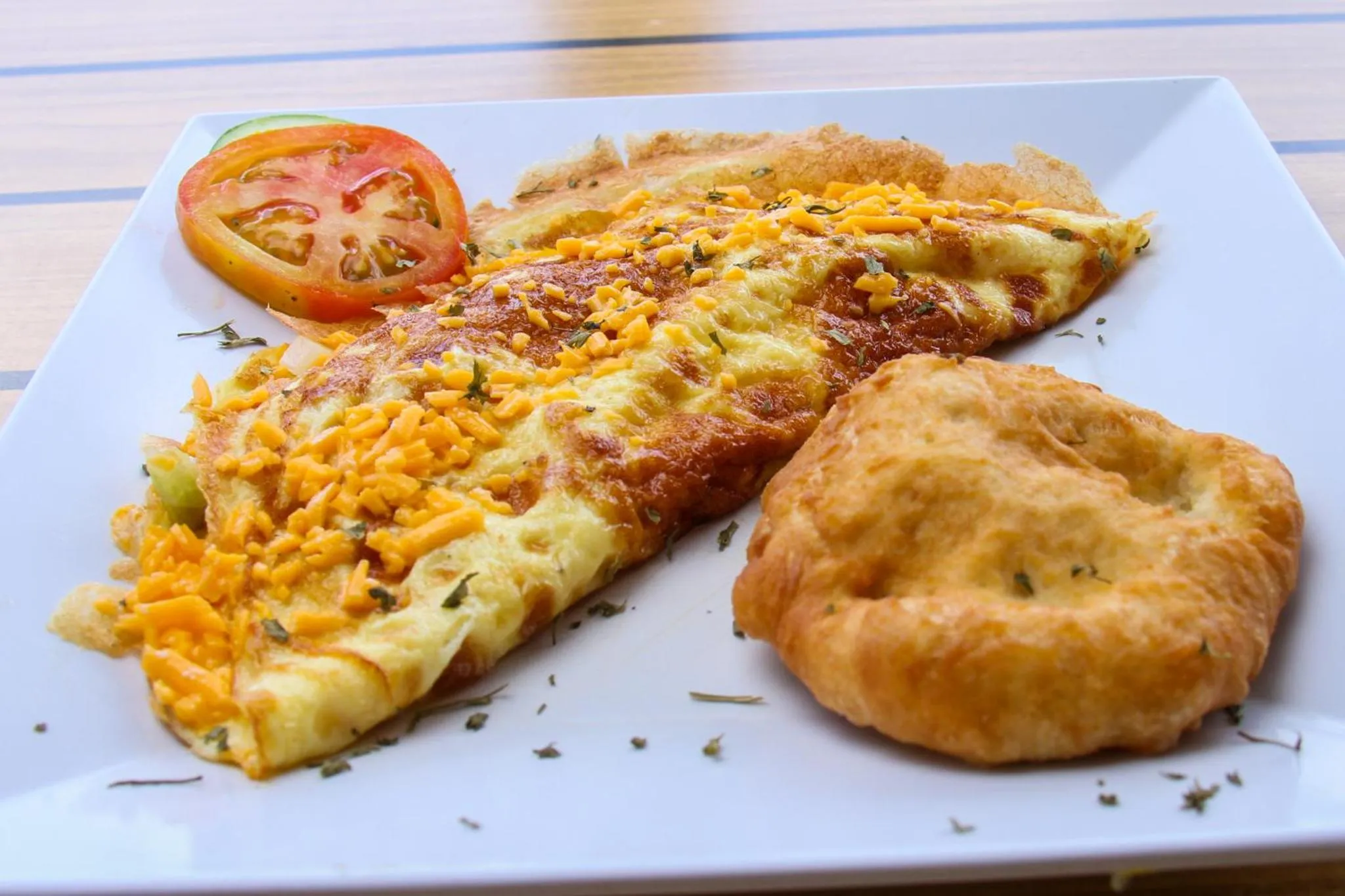 Une assiette garnie d'une omelette au fromage, de tranches de tomate et d'une galette.