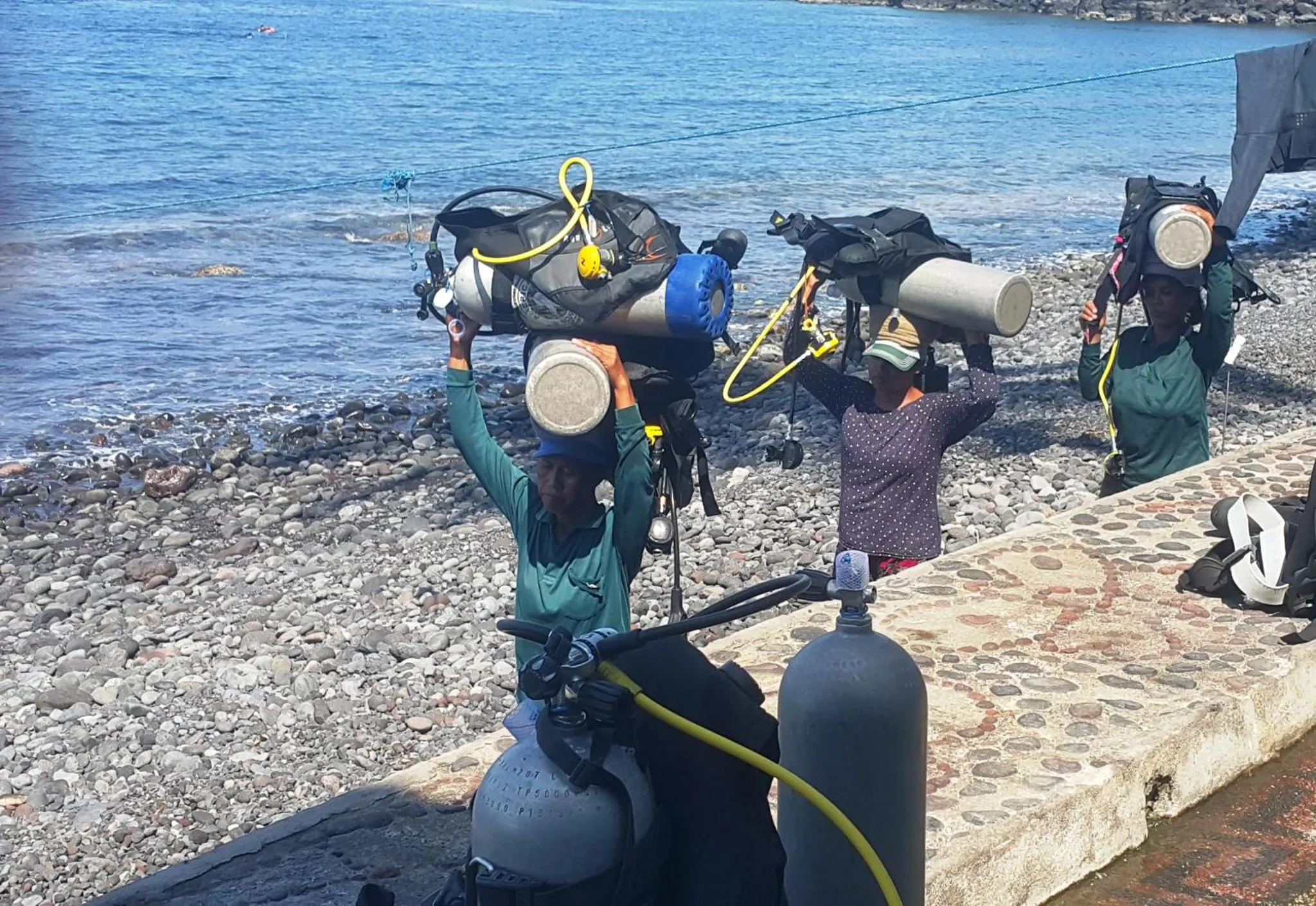 Des personnes transportent des équipements sur un quai rocheux en bord de mer.