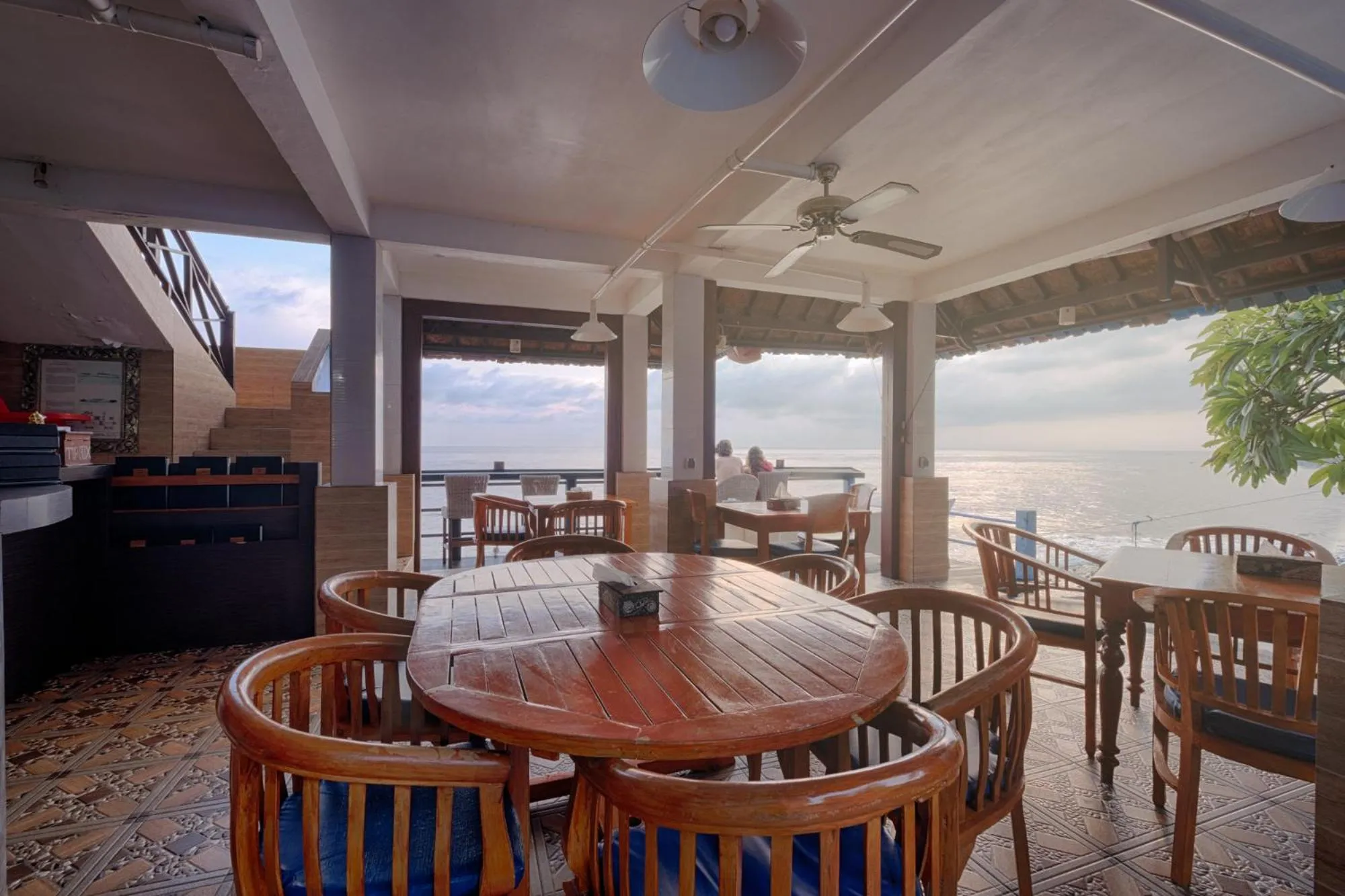 Une salle à manger extérieure avec des tables en bois et une vue sur la mer.