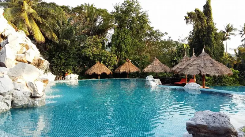 Une piscine turquoise bordée de rochers et de végétation tropicale.