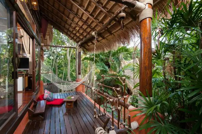 Terrasse en bois avec hamac et végétation luxuriante.