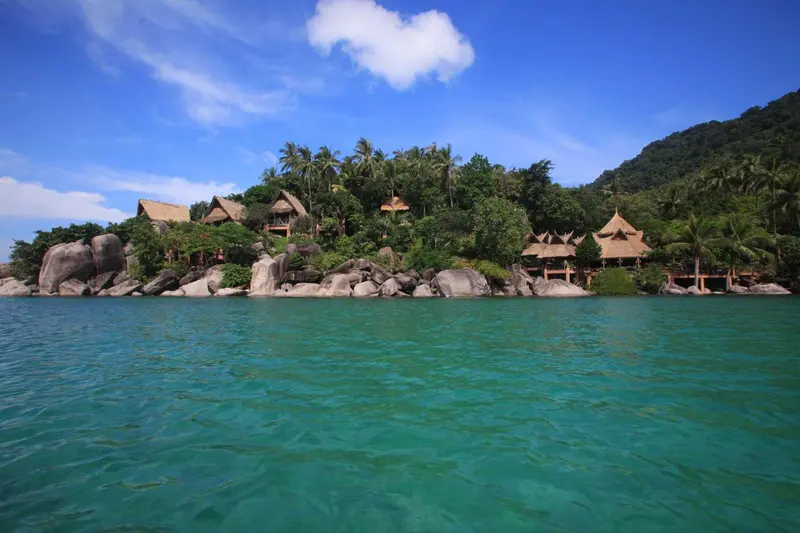 Vue d'une plage tropicale avec des bungalows de chaume et une eau turquoise.