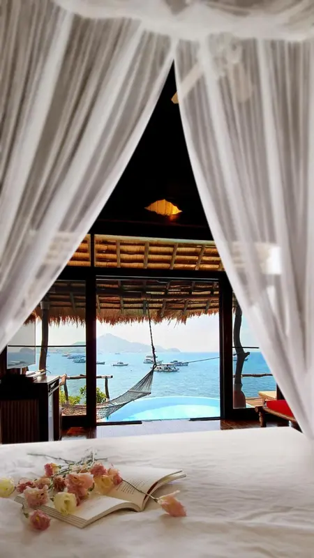 Un lit defait surplombe une vue sur la mer et une piscine.