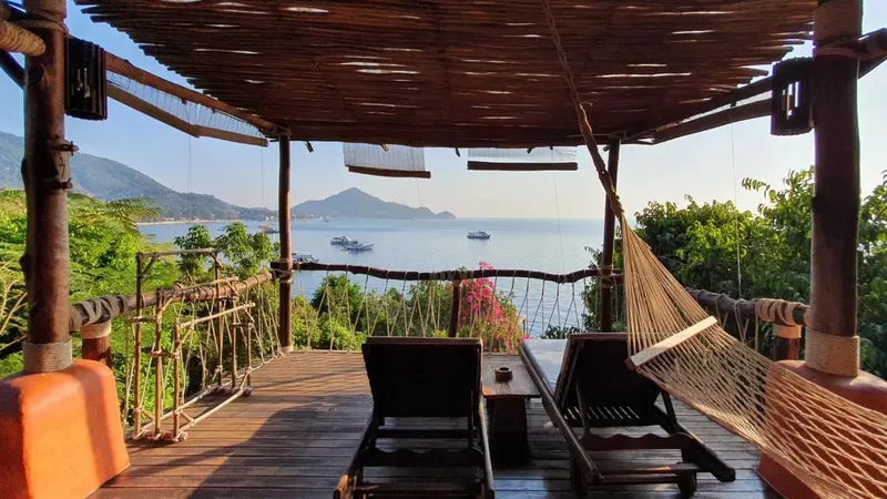Terrasse en bois avec hamac et mobilier de détente donnant sur une vue panoramique sur la mer.