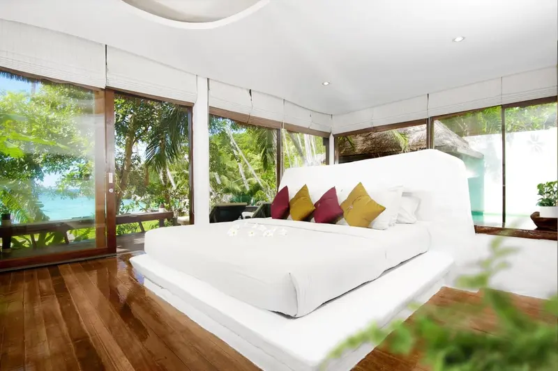 Une chambre lumineuse avec un grand lit blanc et une vue sur la végétation tropicale.