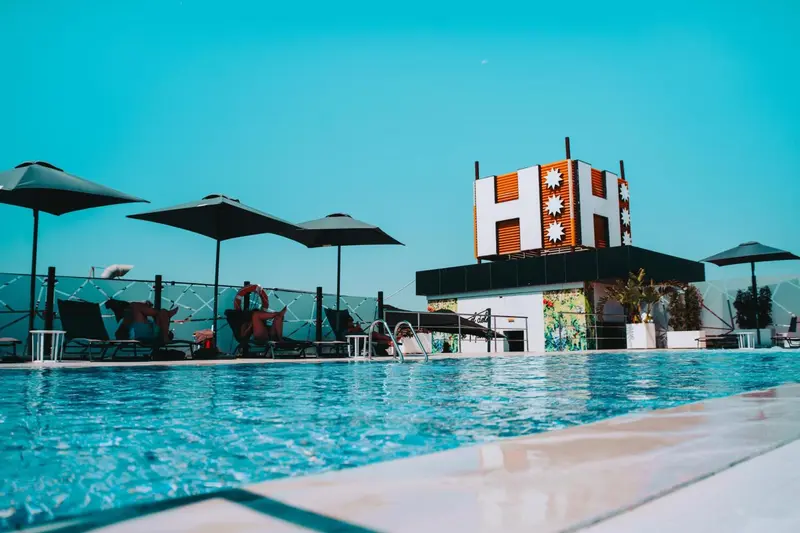 Une piscine turquoise bordée de transats sous des parasols noirs.