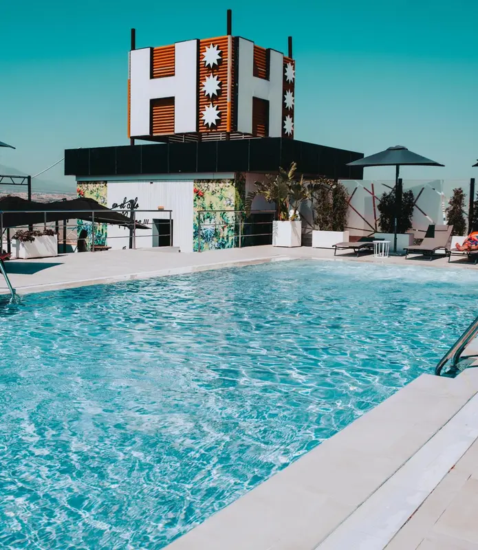 Une piscine turquoise avec un grand panneau lumineux en forme de H au fond.