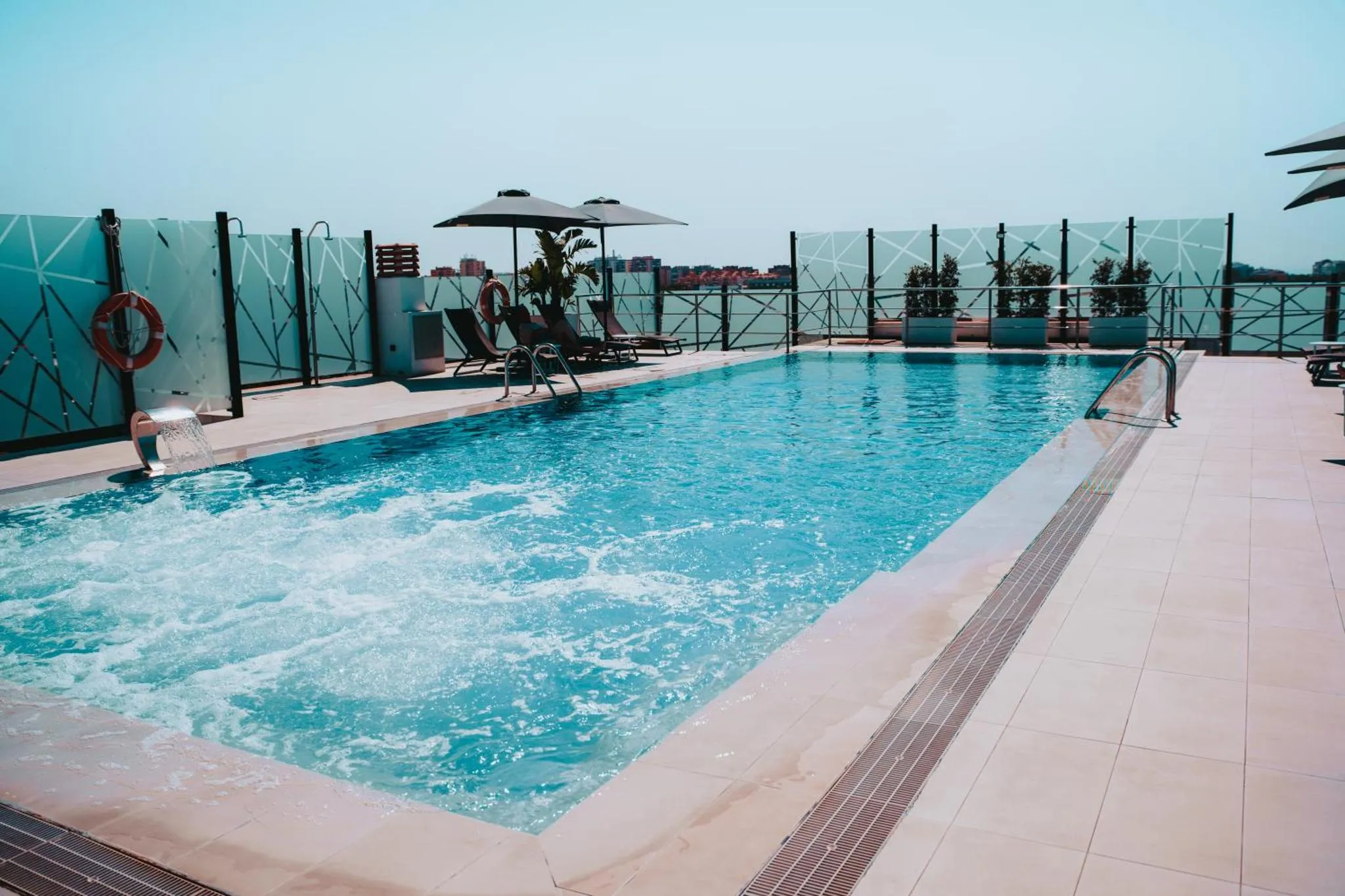 Piscine rectangulaire sur une terrasse ensoleillée avec transats et parasols.