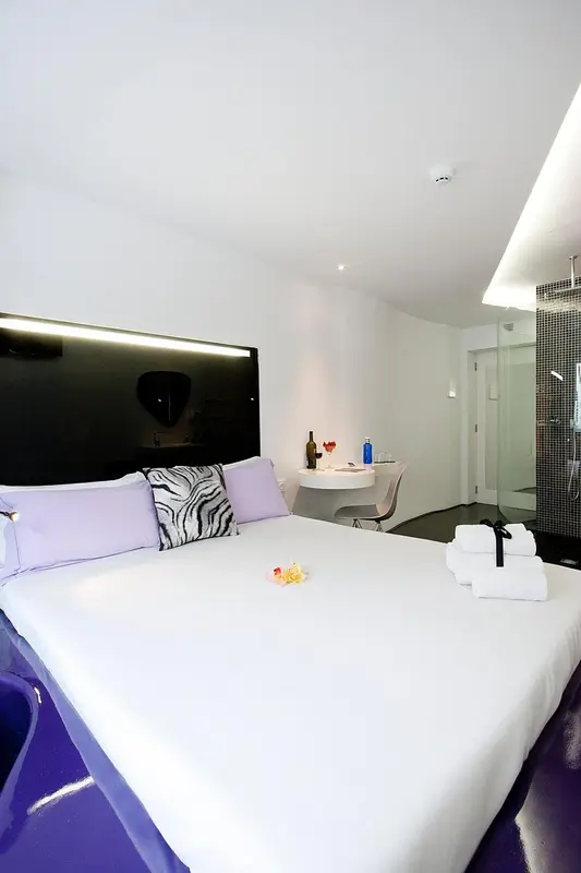 Une chambre lumineuse avec un grand lit recouvert de draps blancs et de coussins violets.