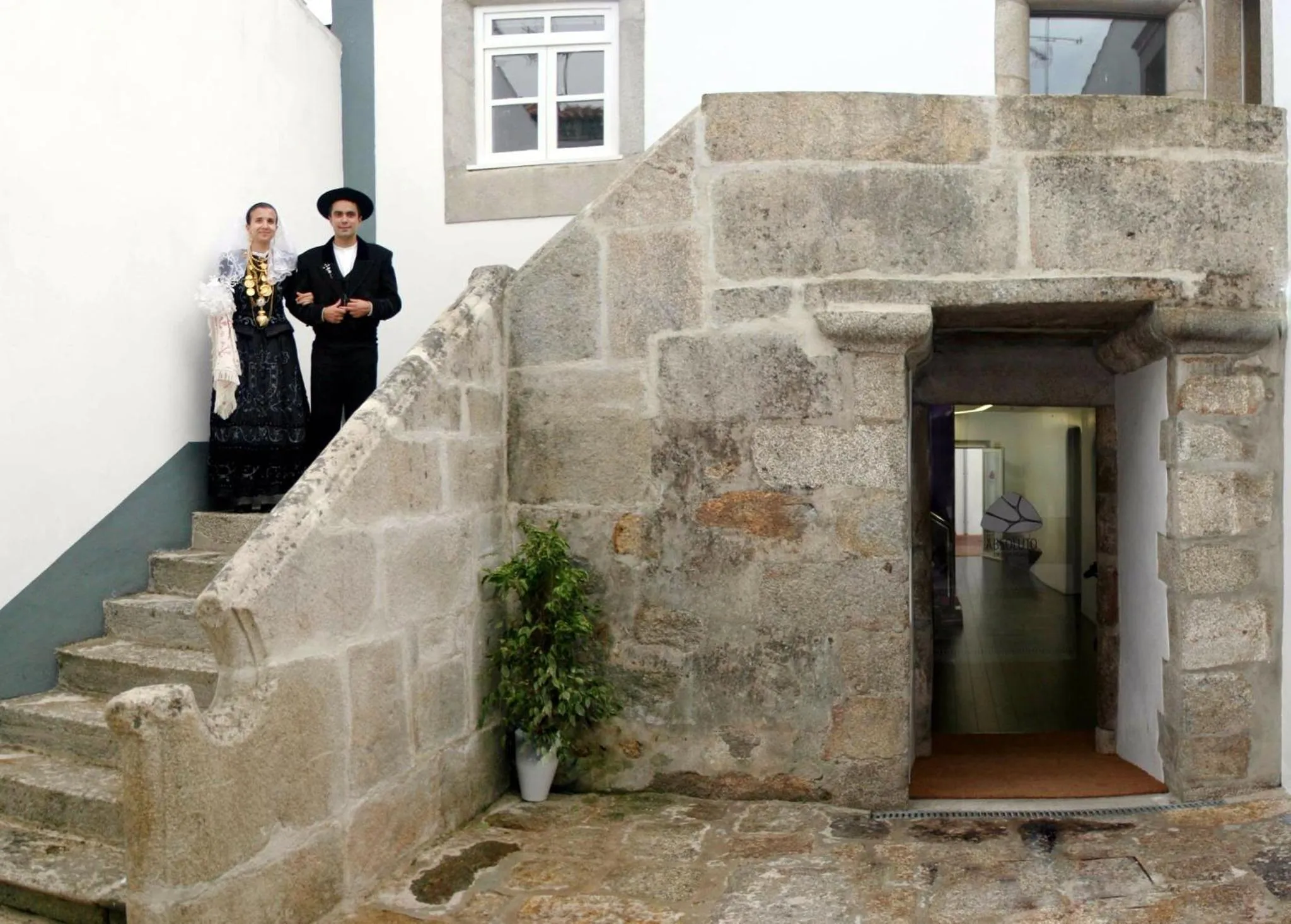 Deux personnes en costumes traditionnels se tiennent devant un escalier en pierre menant à une entrée.