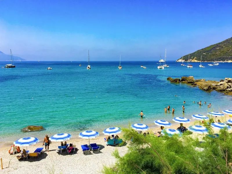 Une plage de sable avec des parasols et des transats face à une mer turquoise.