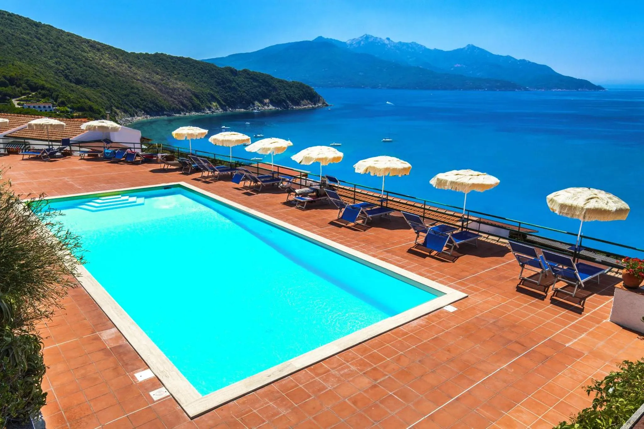 Terrasse avec piscine et transats face à la mer et aux montagnes.