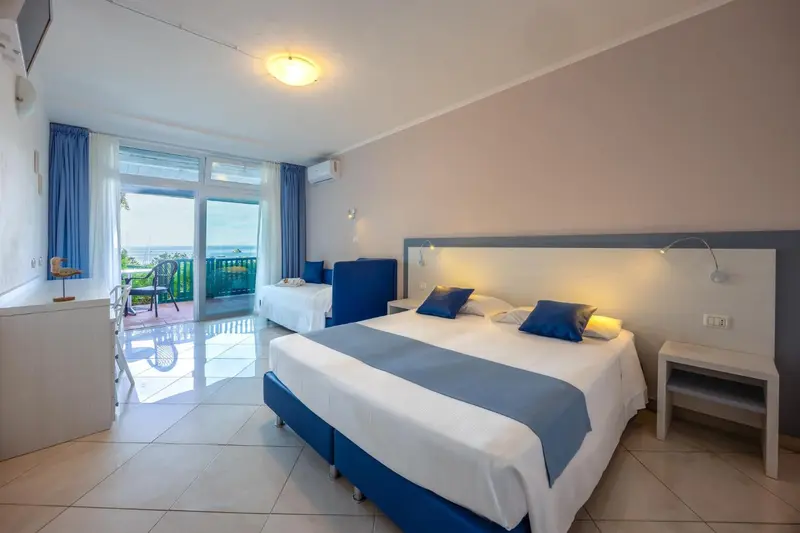 Chambre lumineuse avec lits jumeaux et vue sur la mer depuis un balcon.