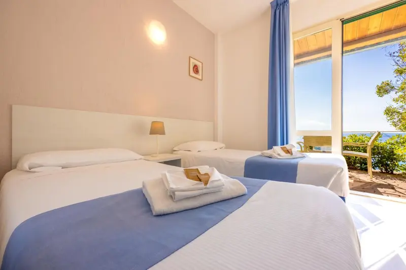 Chambre lumineuse avec deux lits simples et vue sur la mer.