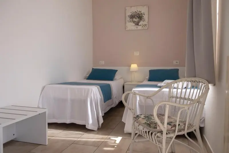 Une chambre lumineuse avec deux lits simples et une chaise en rotin.