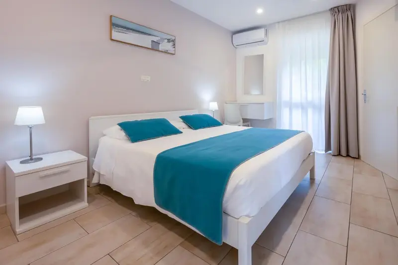 Une chambre lumineuse avec un grand lit recouvert d'une courtepointe turquoise.