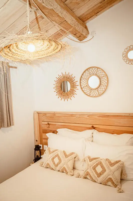 Une chambre lumineuse avec un lit recouvert d'oreillers décoratifs et des éléments de décoration murale en rotin.