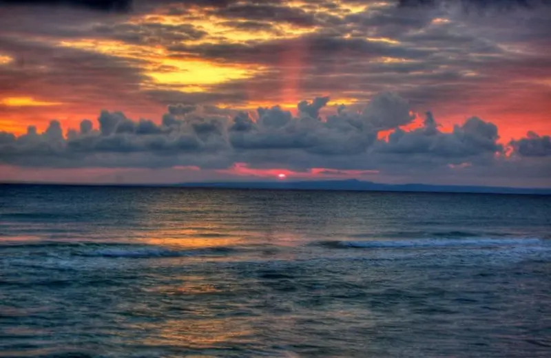 Un coucher de soleil flamboyant illumine l'océan et le ciel nuageux.