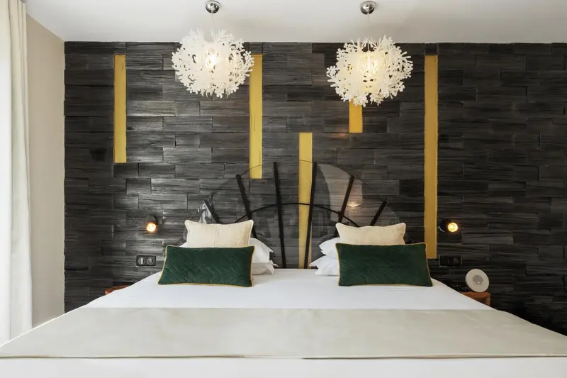 Un lit double avec des oreillers verts et blancs dans une chambre décorée de panneaux muraux sombres et de luminaires blancs.