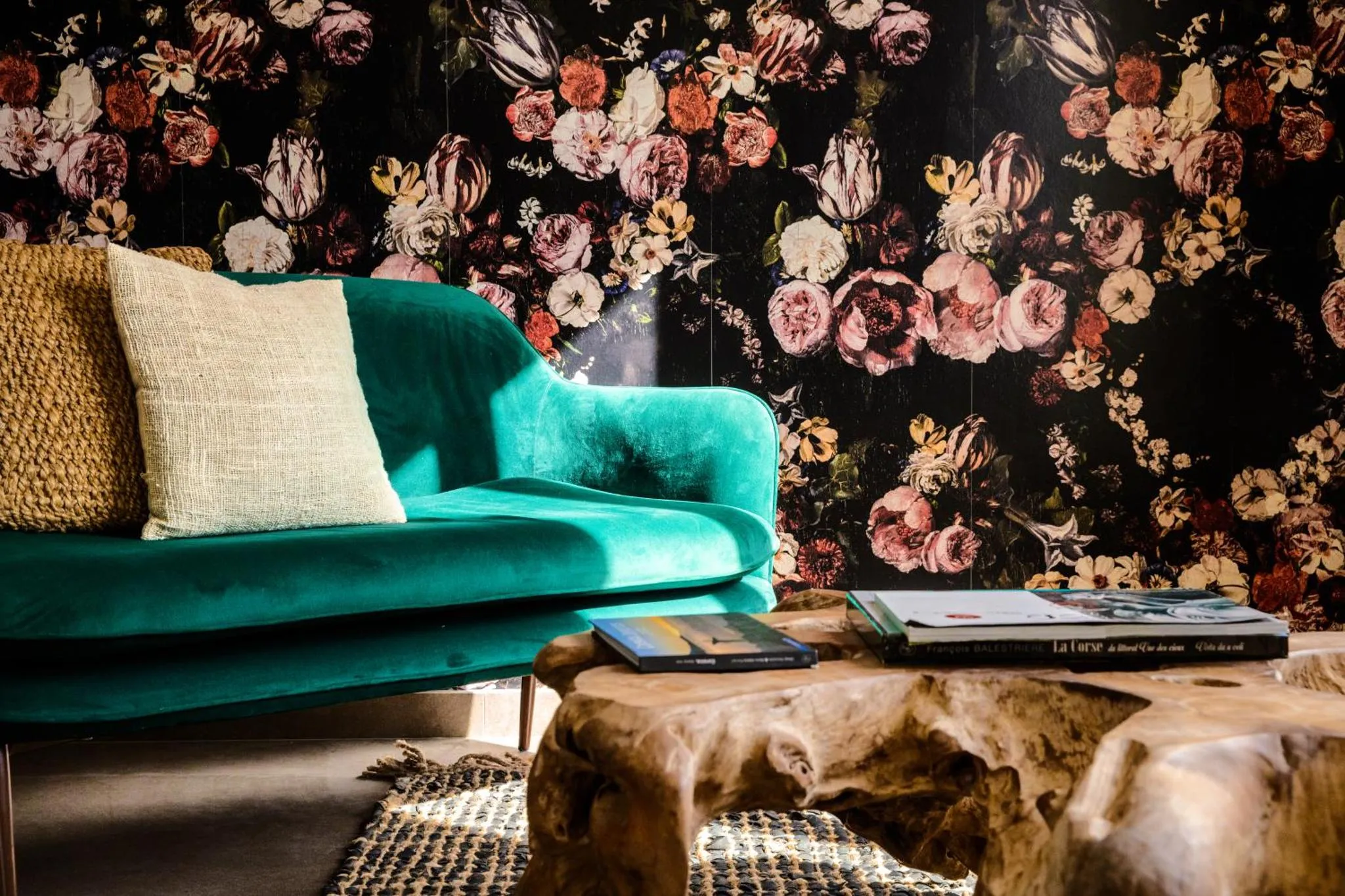 Un canapé turquoise et des coussins reposent devant un mur floral foncé.