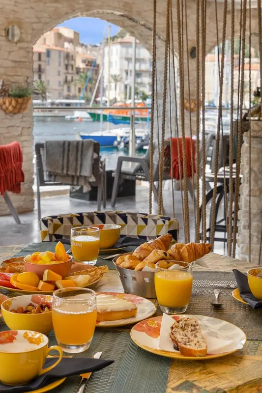 Une table est dressée pour le petit-déjeuner avec des fruits, des viennoiseries et du jus d'orange.