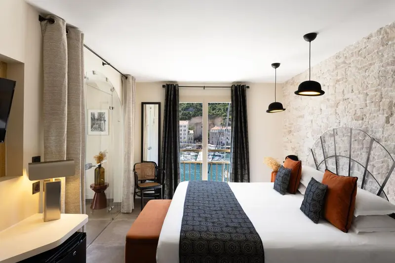 Chambre lumineuse avec un lit double et vue sur un port.