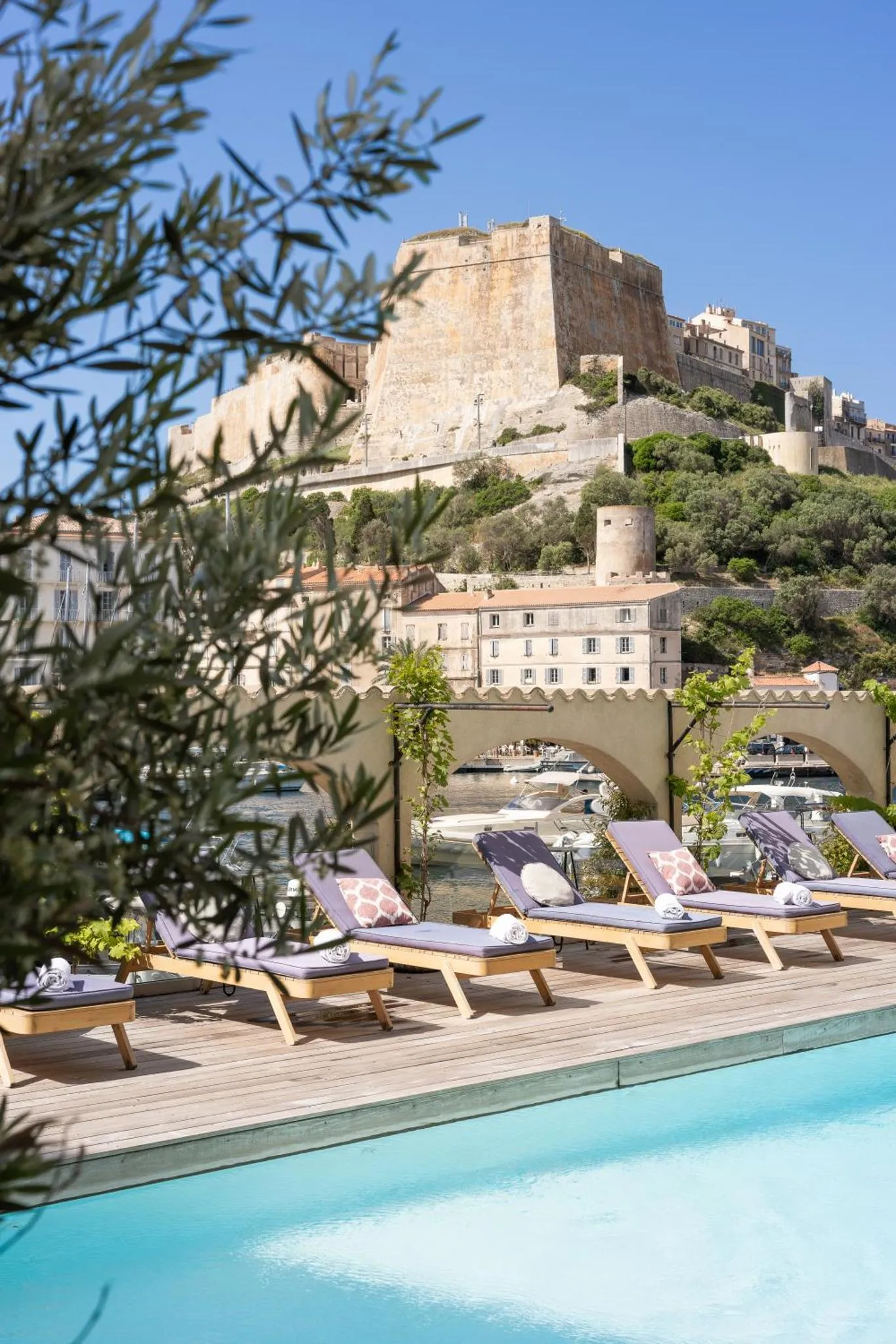Transats roses au bord d'une piscine avec vue sur un château et la mer.