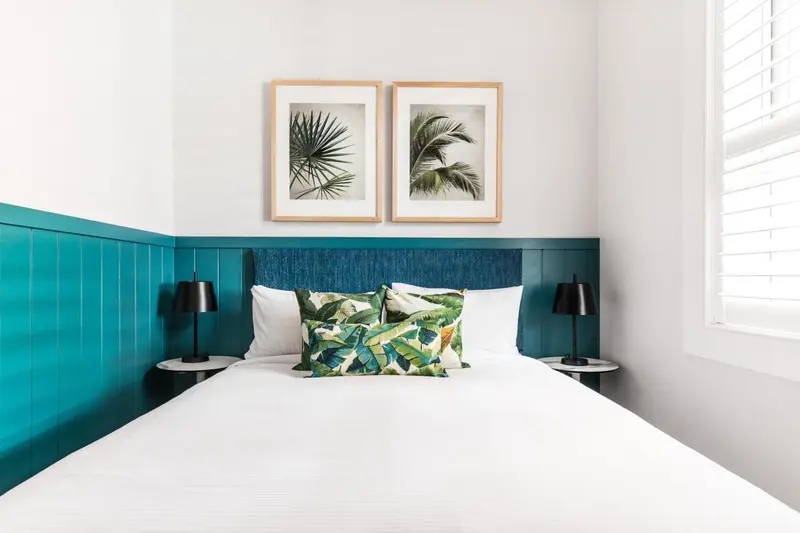Une chambre lumineuse avec un grand lit recouvert d'une courtepointe blanche et de coussins à motifs.