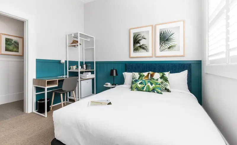 Une chambre lumineuse avec un lit recouvert d'une courtepointe blanche et de coussins décoratifs.