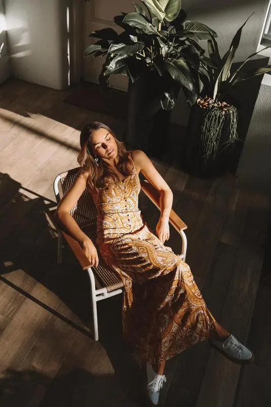 Une femme est assise sur une chaise en osier dans un intérieur lumineux.