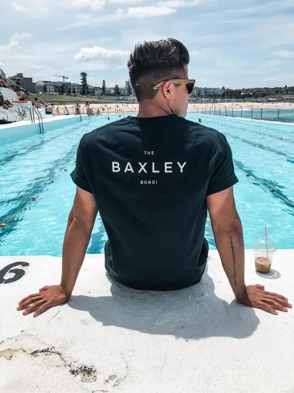 Un homme est assis au bord d'une piscine turquoise, face à l'océan.