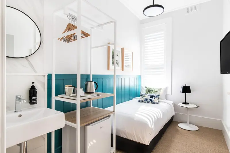Une chambre lumineuse avec un lit simple et un coin lavabo.
