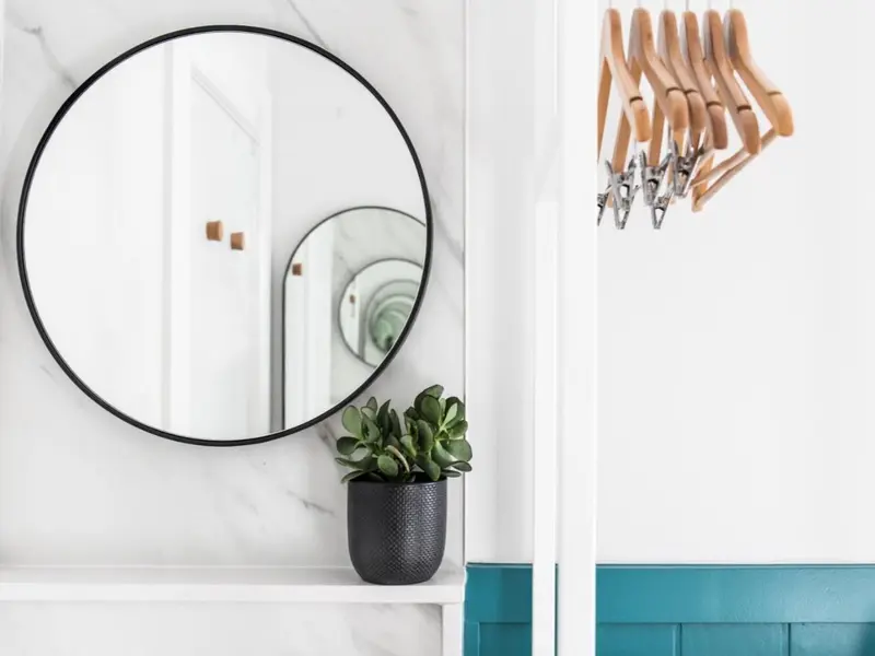 Un miroir rond au-dessus d'une étagère avec une plante verte.