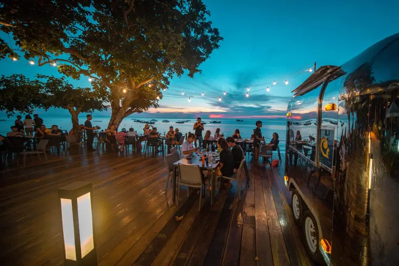 Une terrasse lumineuse avec des tables et des chaises face à la mer au coucher du soleil.