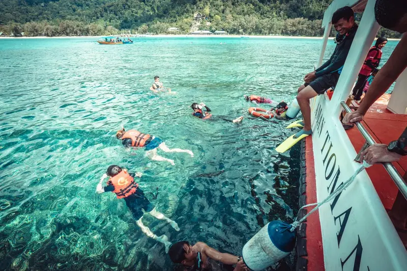 Des personnes en gilets de sauvetage se baignent dans une eau turquoise depuis un bateau.