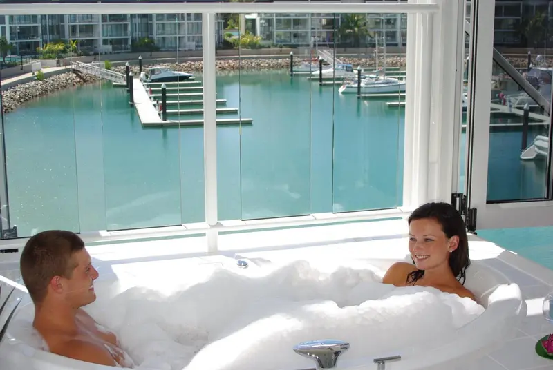 Un couple se détend dans un jacuzzi avec vue sur un port de plaisance.
