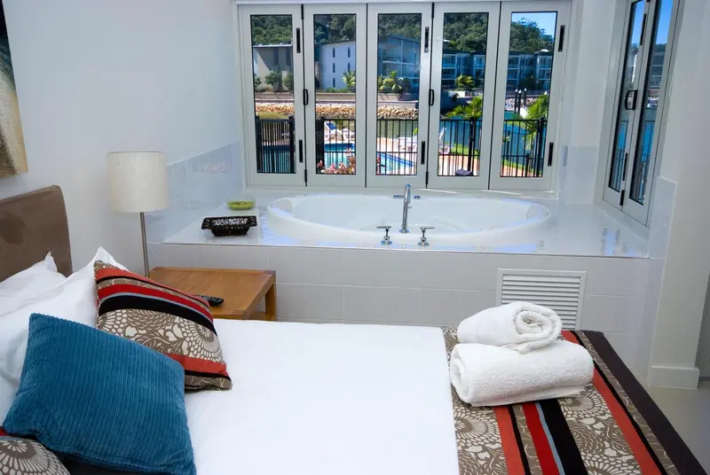 Une chambre lumineuse avec un grand lit et une baignoire intégrée près d'une fenêtre.